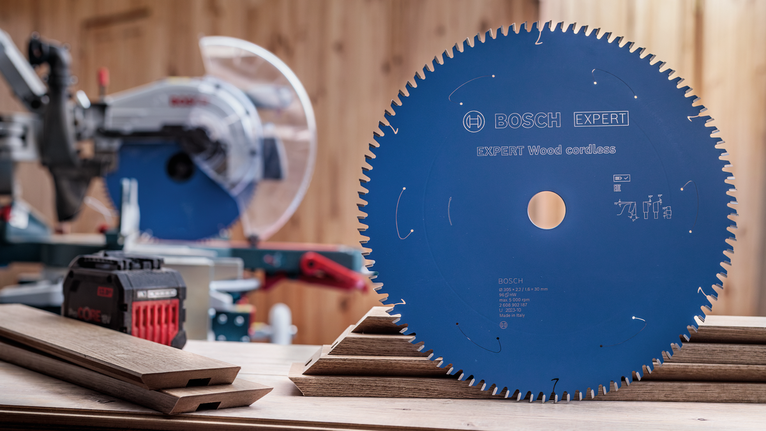 Blue circular saw blade displayed upright on a table beside stacked wooden planks.