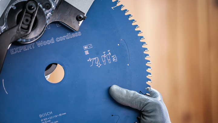 Person wearing safety equipment holding a blue circular saw blade.