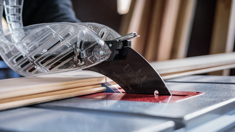 Circular saw cutting wooden planks on a workbench under a transparent safety guard.