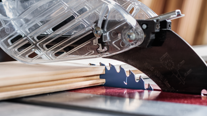 Table saw with a protective guard making precision cuts in a piece of wood.