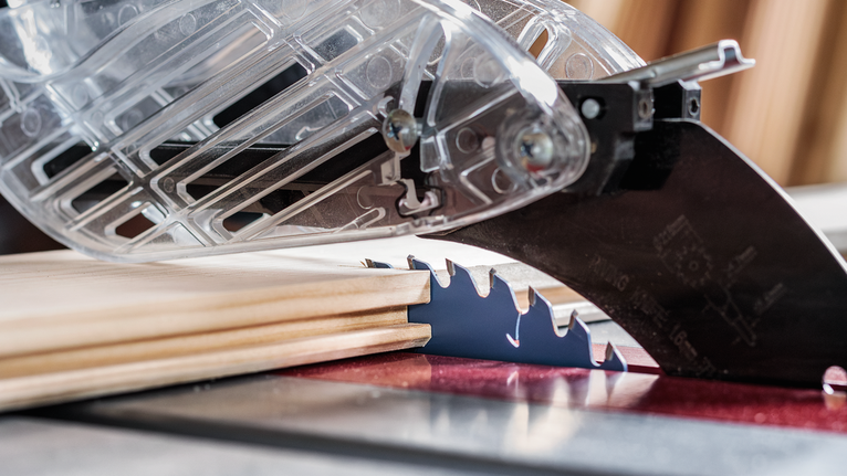 Table saw with a protective guard making precision cuts in a piece of wood.