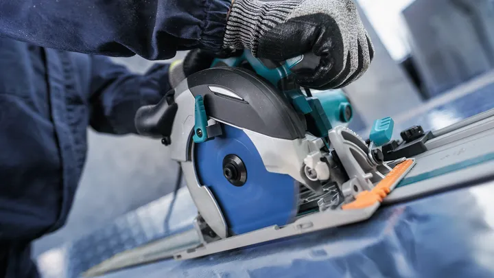 Person wearing safety equipment guides a circular saw to cut a metal sheet.
