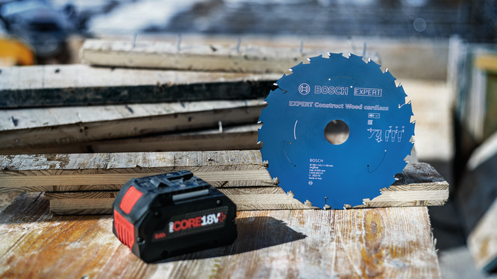Circular saw blade and power tool battery resting on stacked wooden planks.