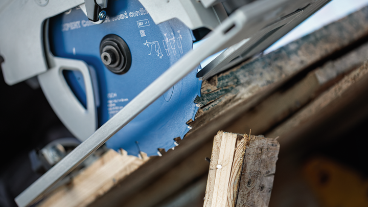 Circular saw blade cutting through a wooden plank outdoors.