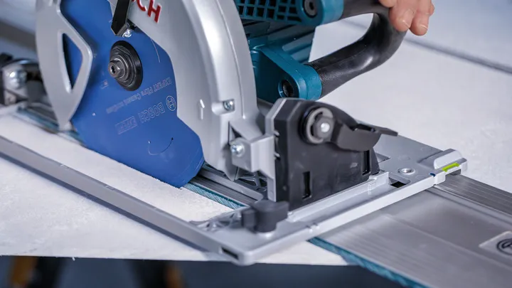 Person guiding a circular saw along a track to cut a tile.