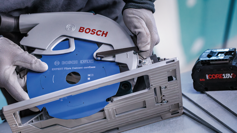 Person wearing safety equipment adjusts a circular saw with a blue blade.