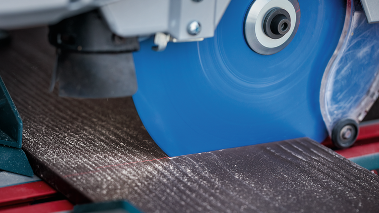 Tile cutting machine slicing through a ceramic tile along a marked line.