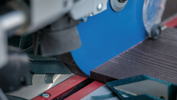 Circular saw cutting through a dark wooden plank in a workshop.