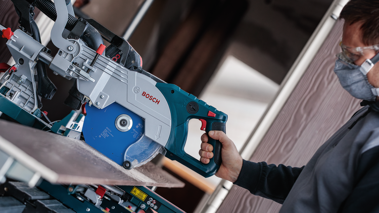 Person wearing safety equipment cuts a tile with a circular saw.