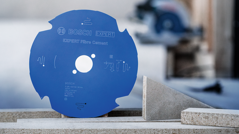 Blue saw blade positioned upright on a concrete block near cut fiber cement pieces.