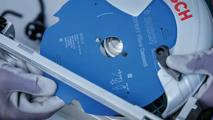 Person wearing safety equipment installs a blue circular saw blade into a power tool.