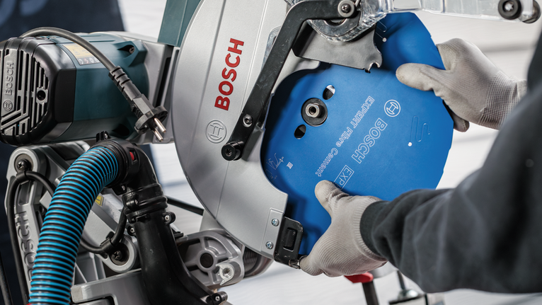 Person wearing safety equipment installs a circular saw blade in a cutting machine.