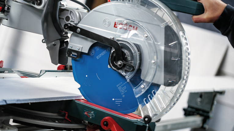 Person operating a circular saw cuts a tile on a workstation.