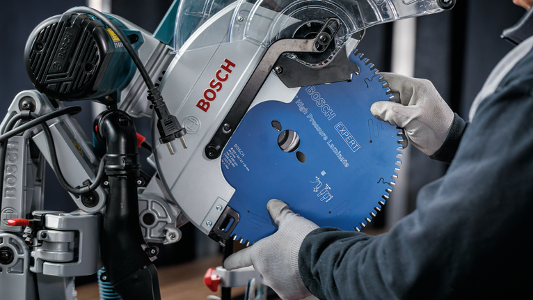 Person wearing safety equipment installs a large circular saw blade into a cutting machine.