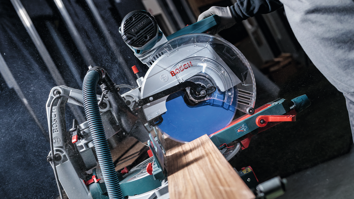 Person wearing safety equipment cuts a wooden board with a miter saw.