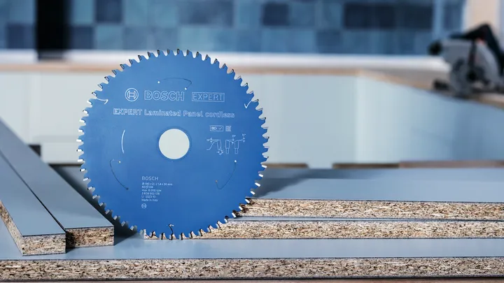 Circular saw blade standing upright on stacked laminated panels in a workshop.
