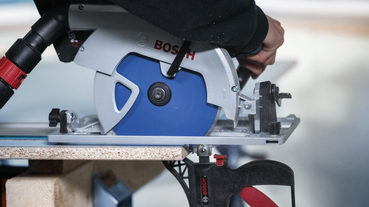 Person operates a circular saw to cut wood, wearing safety equipment.