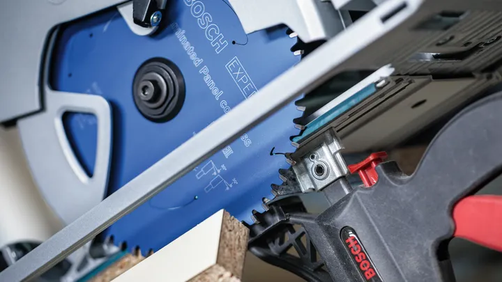 Circular saw cutting through particle board clamped to a workbench.