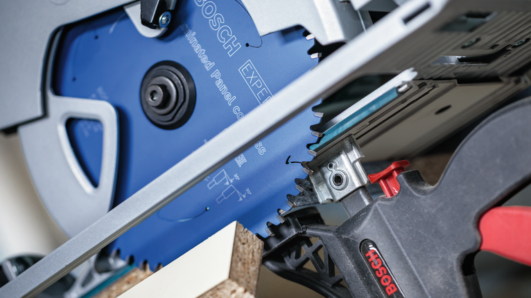 Circular saw cutting through particle board clamped to a workbench.