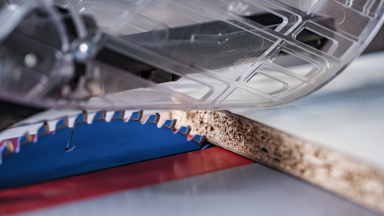 Circular saw blade cutting through a sheet of particle board.
