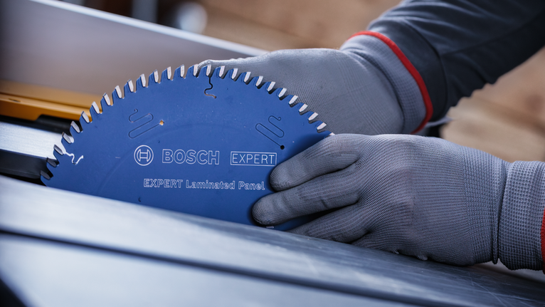 Person wearing safety equipment installs a blue circular saw blade into a table saw.