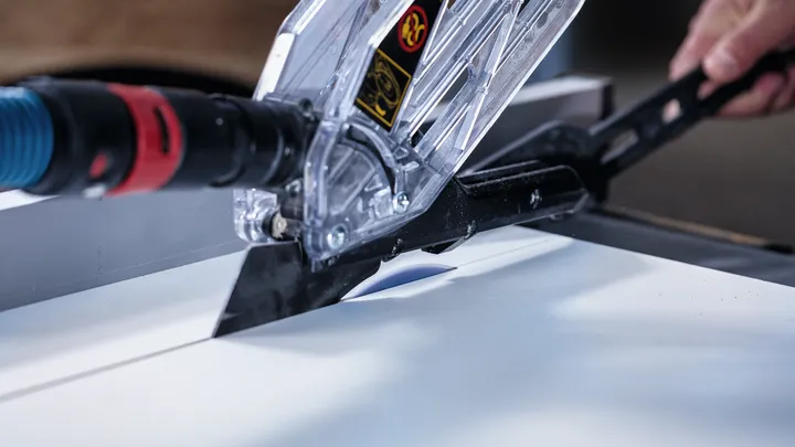 Person guiding a circular saw with dust extraction while cutting a smooth white board.