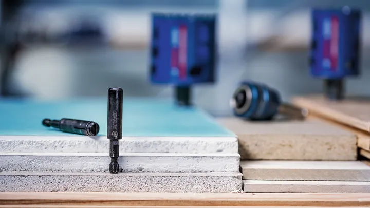 Drill bits and a driver tool placed upright on stacked construction panels.