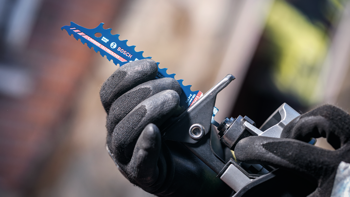 Person wearing safety equipment inserts a saw blade into a power tool.