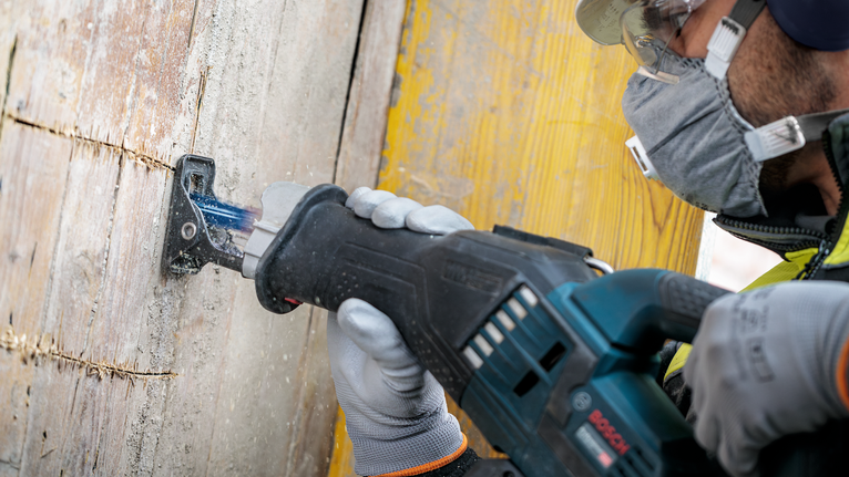 Person wearing safety equipment cuts wooden board with a reciprocating saw.