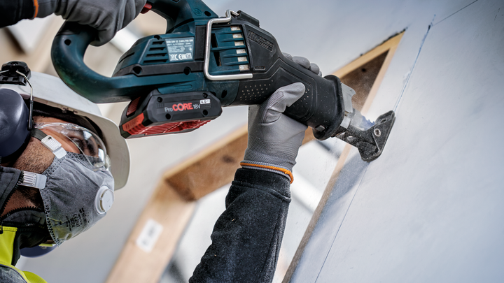 Person wearing safety equipment cuts drywall with a reciprocating saw.