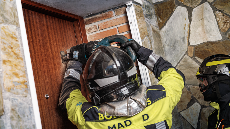 Person wearing safety equipment operates a power tool to cut open a wooden door.