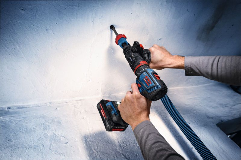 A person drills into a concrete wall with a cordless drill and dust extraction attachment.