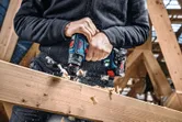 A person drills into a wooden beam using a cordless combi tool.
