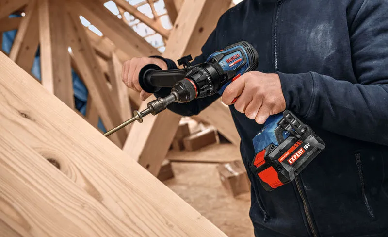 A person uses a cordless drill driver to fasten a screw into wooden beams.