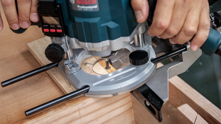 Person operates a power router trimming the edge of a wooden board.