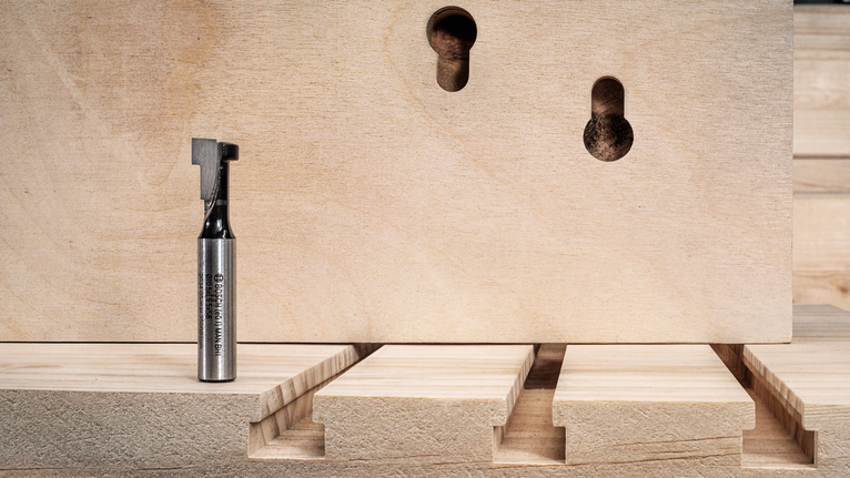 Router bit placed on wood, with precise grooves and keyhole slots cut into the board.