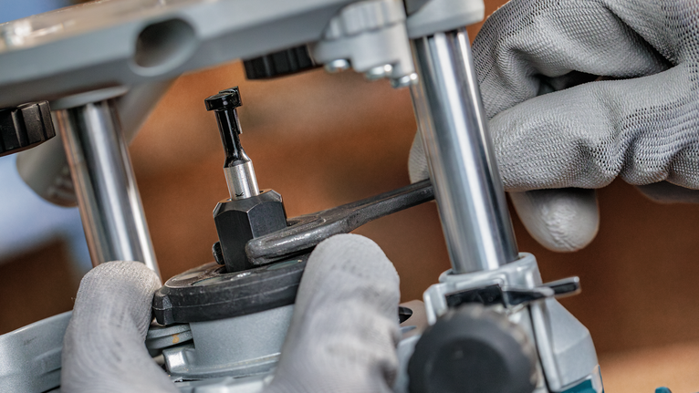 Person wearing safety equipment tightens a router bit using a wrench.