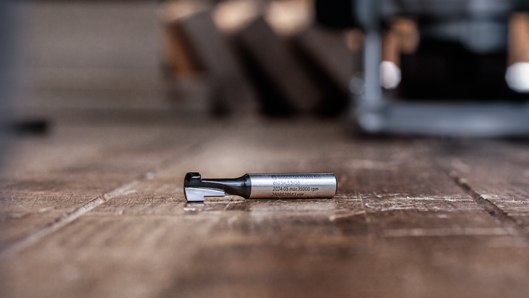 Router bit placed on a wooden floor in a workshop setting.