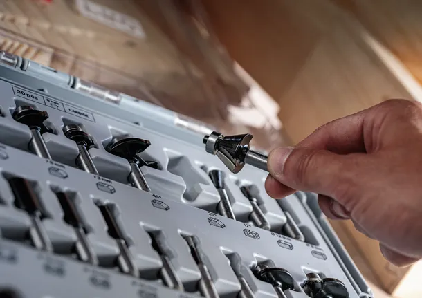 Person selects a drill bit from an organized set in a workshop environment.