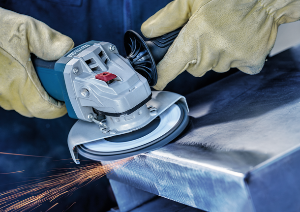 Person wearing safety equipment grinds a metal edge with a power tool.