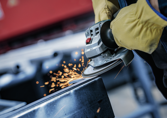 Person wearing safety equipment grinds metal, producing sparks.