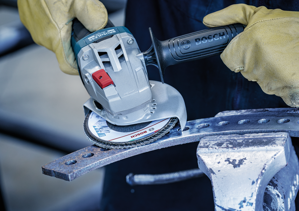 Person wearing safety equipment grinds a metal beam with an angle grinder.