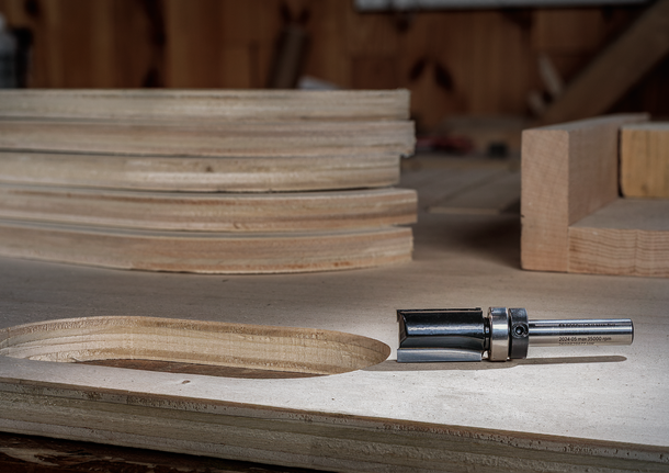 Wood router bit next to a freshly cut opening in stacked plywood sheets.