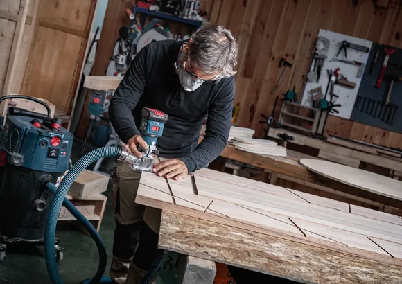 Person wearing safety equipment uses a router to carve grooves on a wooden board.