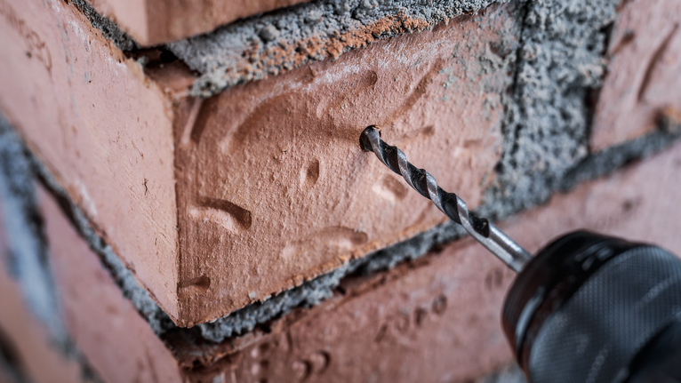 Drill making a hole in a red brick wall.