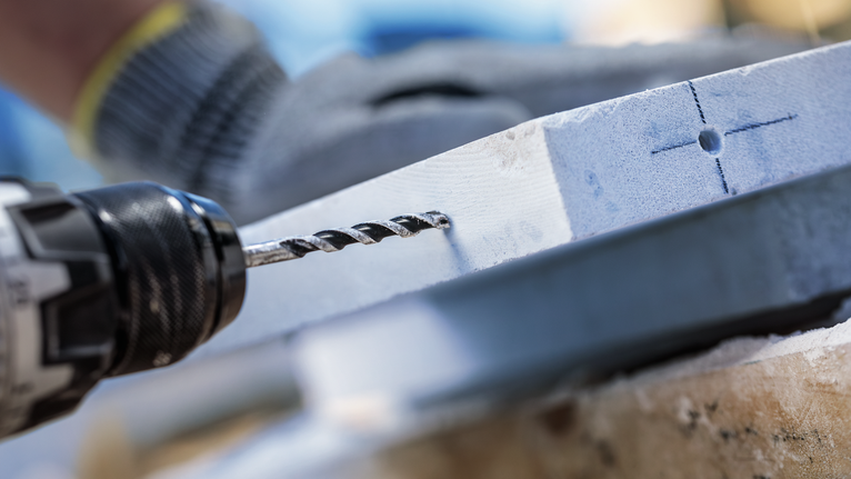Person wearing safety equipment drills a marked hole into a light-colored slab.