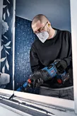 A person wearing safety equipment cuts a window frame with a cordless reciprocating saw.