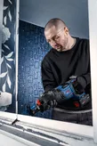 Person wearing safety equipment cuts a window frame with a cordless reciprocating saw.