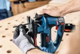 A person wearing safety equipment attaches a blade to a cordless jigsaw.
