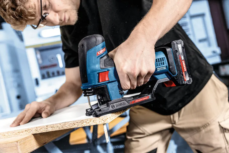 A person operates a jigsaw to cut a piece of particle board.